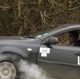 A grey Daewoo Lacetti driving off-road through woodland on a car trial, exhaust smoke rising